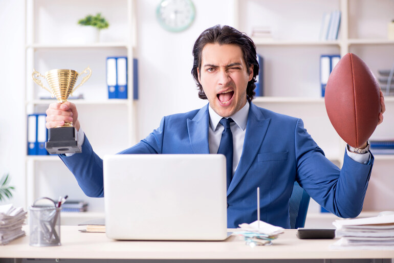 Excited man at desk holding trophy and football, symbolizing winning bets, sports analysis, and smart wagering tips tailored for a music-loving audience